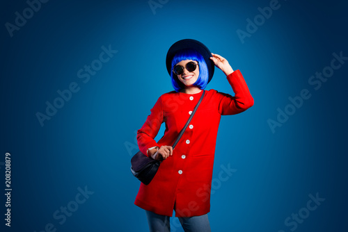 Portrait of cheerful fancy girl in red coat pants having beaming smile resting relaxing posing holding bag on shoulder isolated on vivid blue background