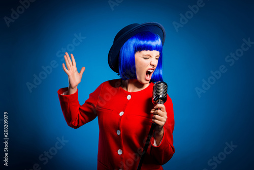 Portrait of professional emotional artist in head wear singing hard rock with wide open mouth and close eyes gesturing with hand isolated on bright blue background. Art jazz opera concept