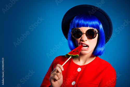 Wallpaper Mural Portrait with copy space empty place of stupid mad girl in headwear glasswear red outfit biting lolli pop on stick with nervous rage expression isolated on blue background Torontodigital.ca