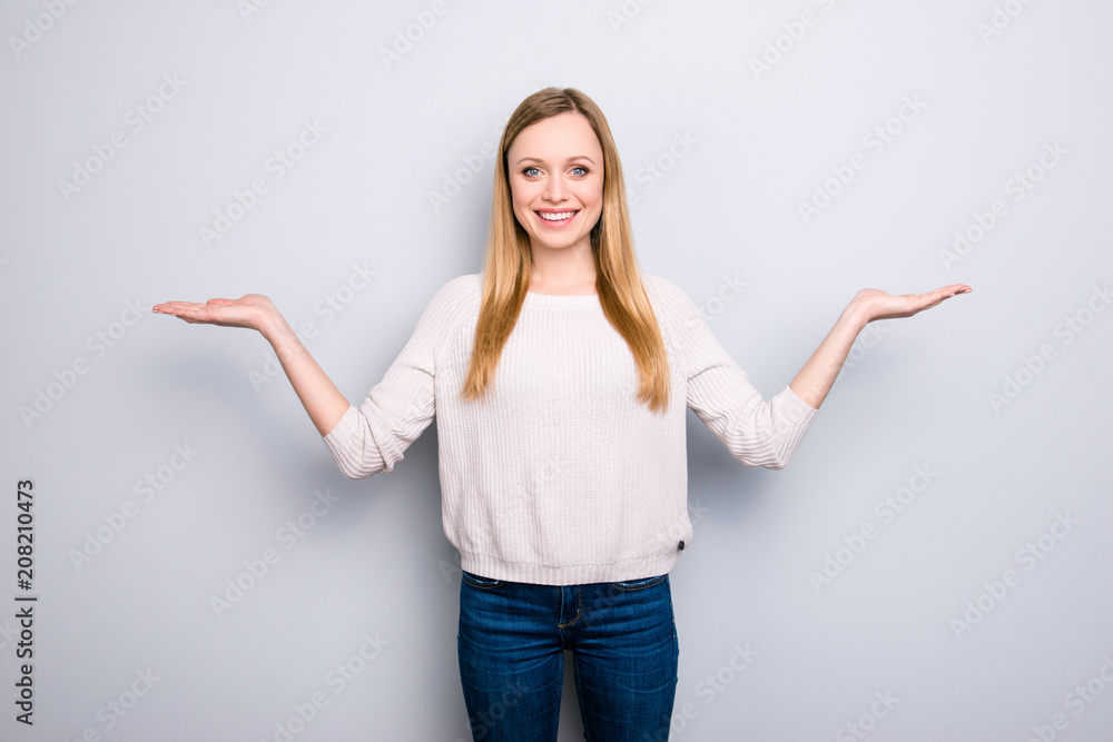 Portrait of stylish trendy girl in jeans sweater holding two copyspace empty places on palms looking at camera isolated on grey background Portrait of stylish trendy girl in jeans sweater holding two copyspace empty places on palms looking at camera isolated on grey background