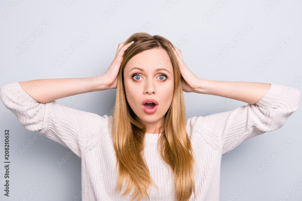 Portrait of curious frustrated girl with wide open mouth holding two hands on head looking at camera isolated on grey background Portrait of curious frustrated girl with wide open mouth holding two hands on head looking at camera isolated on grey background