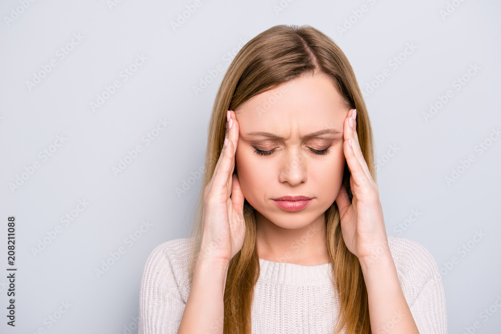 Portrait of unhappy sad girl holding two hands on temples suffering from head ache keeping eyes closed isolated on grey background Portrait of unhappy sad girl holding two hands on temples suffering from head ache keeping eyes closed isolated on grey background