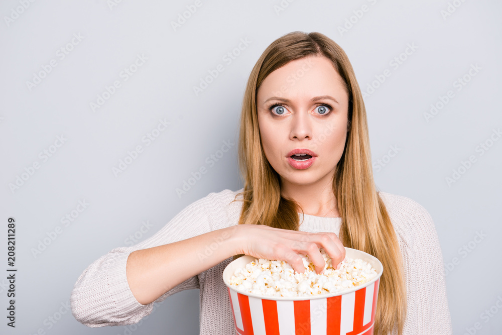 Fototapeta premium Portrait of shocked astonished girl with wide open eyes mouth holding bucket with pop corn looking exciting interesting premier horror film isolated on grey background