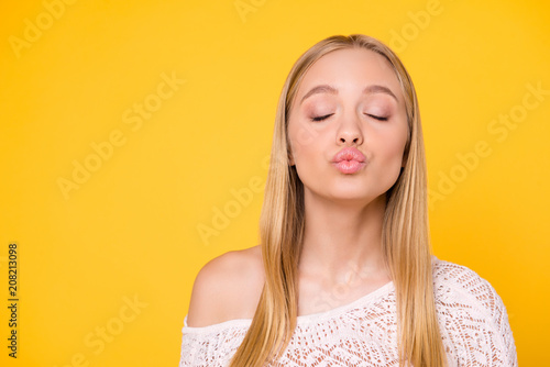 Portrait with copyspace empty place, advertisement concept, lovely  sweet girl keeping eyes closed blowing kiss with pout lips isolated on yellow background