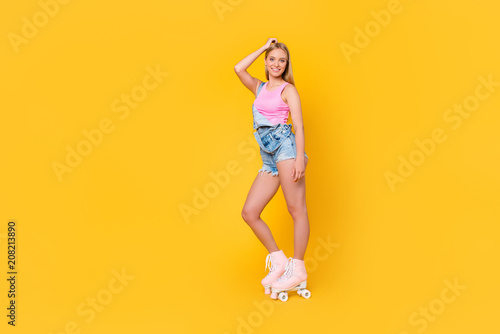 Low angle bottom view portrait of cheerful coquette pretty chick positive sportive girl riding on roller skates looking at camera isolated on yellow background