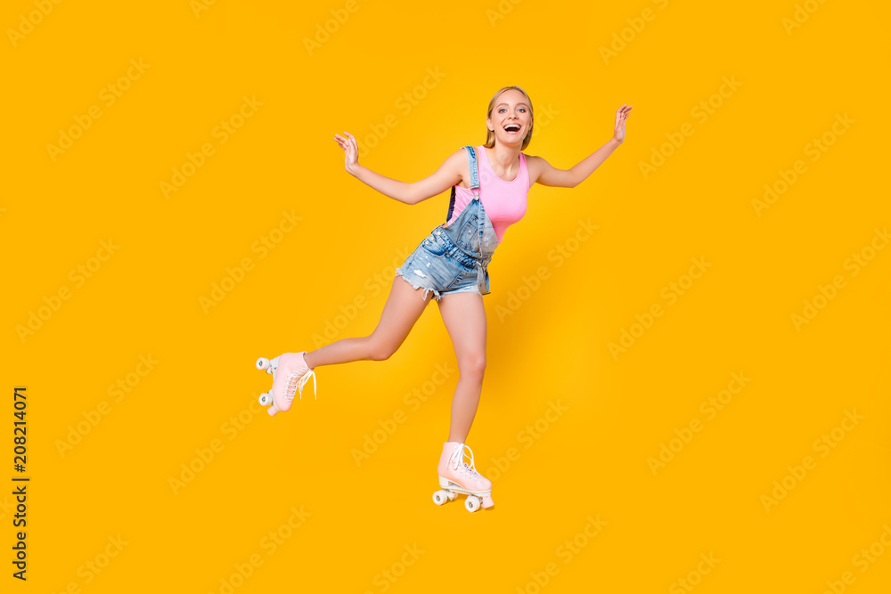 Full-length portrait of glad excited girl riding on roller skates with one leg keeping balance enjoying recreation exercise isolated on yellow background, sporty fit people concept