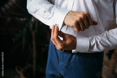 Close-up groom hands hold cufflinks. Elegant gentleman clother, white shirt and black belt. concept of classic work clothes in the office, jewelry.