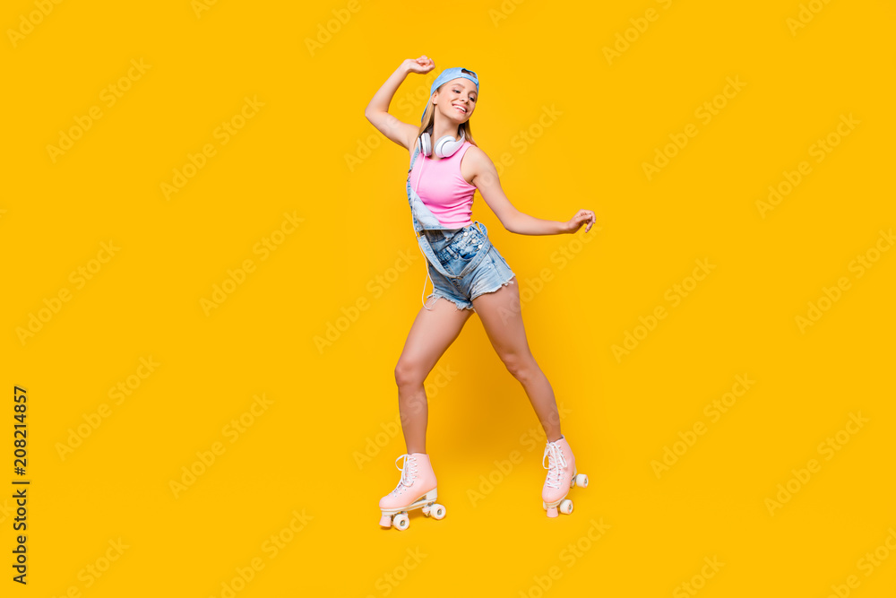 Portrait of fit sporty athletic girl with headset on neck riding on roller skates having pleasure delight listening music chilling isolated on yellow background Portrait of fit sporty athletic girl with headset on neck riding on roller skates having pleasure delight listening music chilling isolated on yellow background