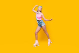 Portrait of fit sporty athletic girl with headset on neck riding on roller skates having pleasure delight  listening music chilling isolated on yellow background