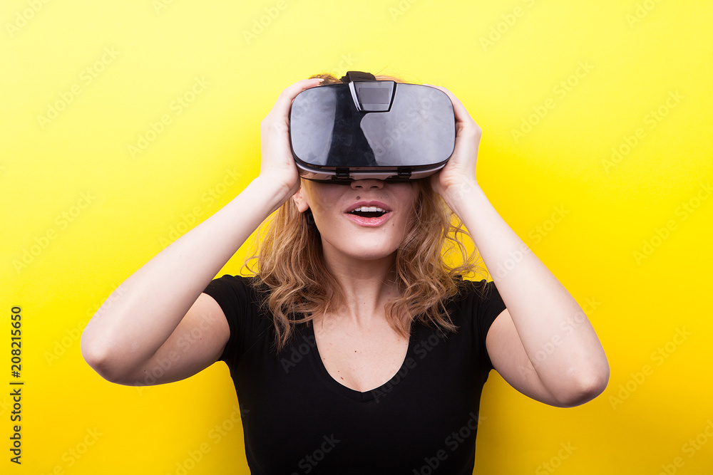 Beautiful woman enjoying virtual reality experience on yellow background in studio photo Beautiful woman enjoying virtual reality experience on yellow background in studio photo