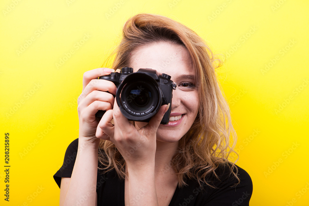 Beautiful woman holds a camera at her eye taking a picture on yellow background in studio photo Beautiful woman holds a camera at her eye taking a picture on yellow background in studio photo