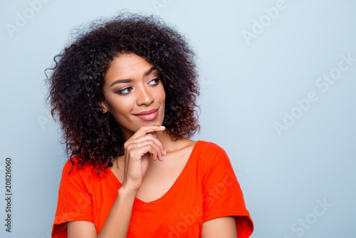 Portrait of minded ponder woman in bright outfit holding hand on chin looking at copy-space with smirk isolated on grey background photo