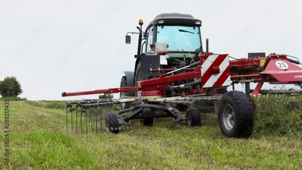 Tractor riding on farm margin with agriculture combine carriage harvesting grass on cloudy summer day Tractor riding on farm margin with agriculture combine carriage harvesting grass on cloudy summer day