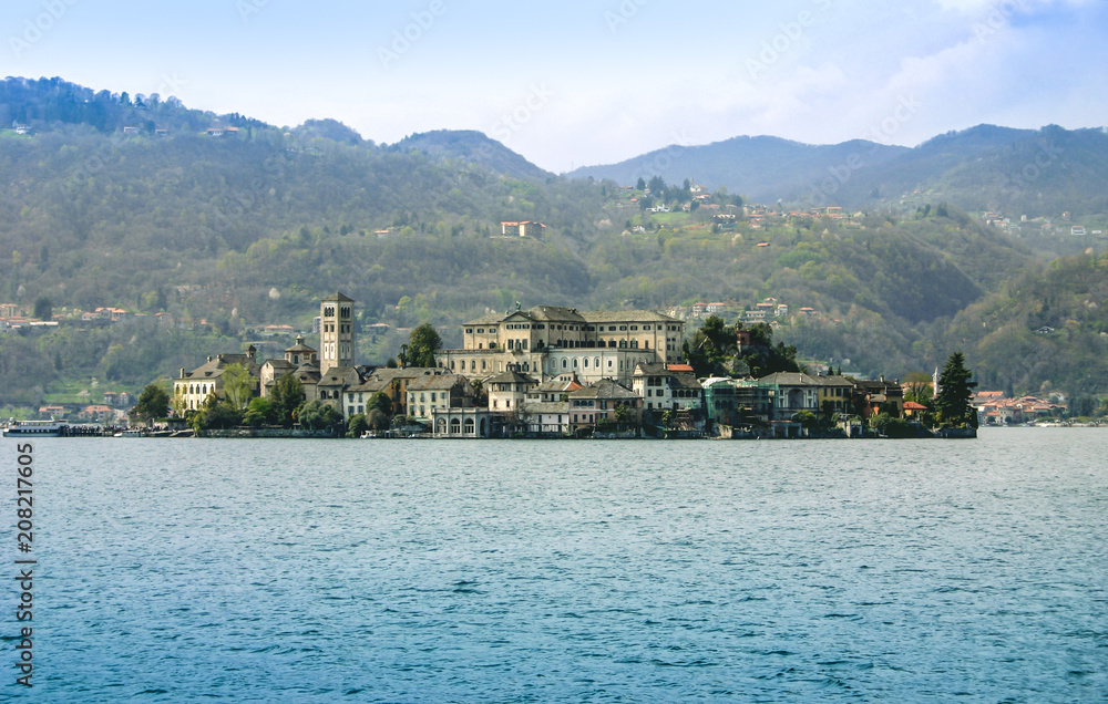Island with the large villa, church and residential buildings in the sea. In the foreground is blue sea water, the focus is the island, in the background are mountains with forest and homes in between