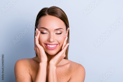 Portrait of pleased satisfied girl touching face enjoying ideal perfect skin after procedure mask keeping eyes closed isolated on grey background photo