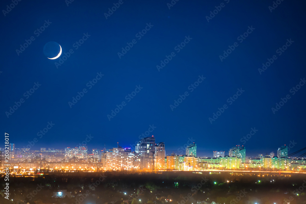 City at night with new moon on dark blue sky with stars