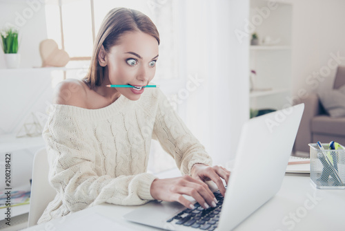 Fotografia Portrait of astonished big-eyed woman holding pen in teeth typing on keypad keyb