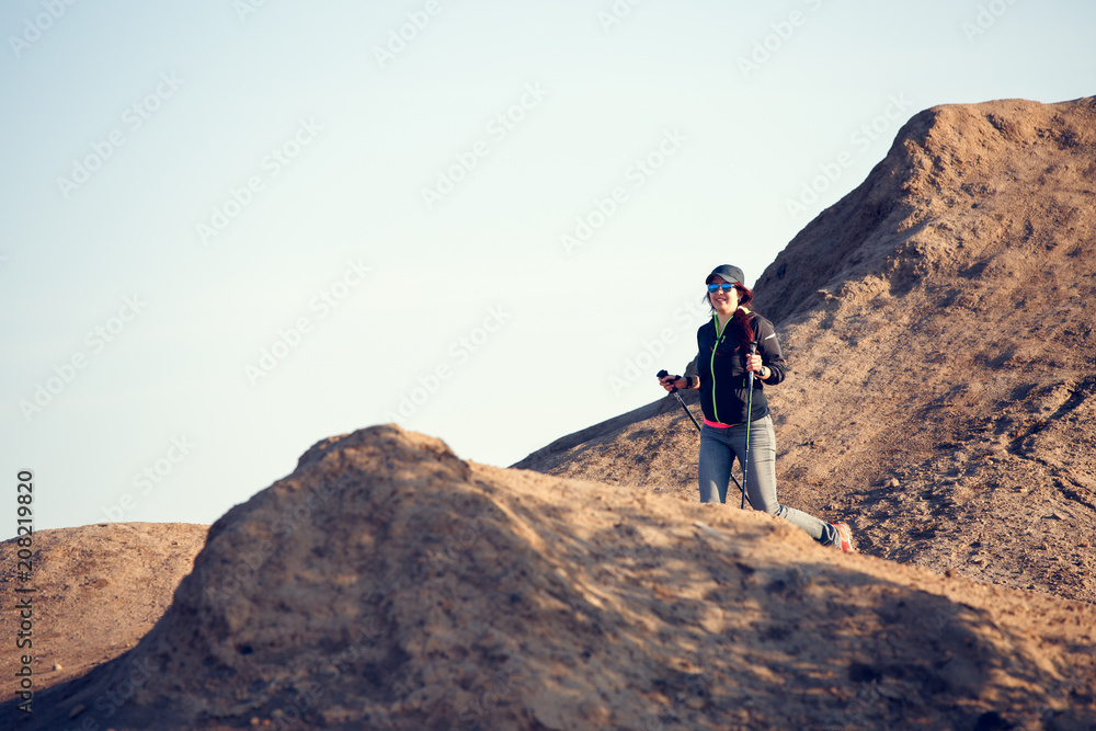 Image in full growth of tourist girl with backpack and sticks for walking on mountain