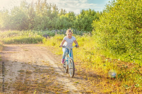 Happy child riding bike. Young girl on bicycle in sunny summer park. Healthy school children summer activity. Kids playing and cycling outdoors. Little girl learns to keep balance while riding bicycle