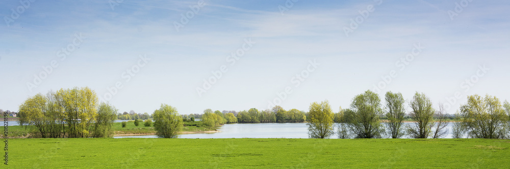 Beautiful view on a typical dutch landscape near the river Waal and Zaltbommel, water, green grass, meadows, floodplains and trees on a sunny day in april, springtime Beautiful view on a typical dutch landscape near the river Waal and Zaltbommel, water, green grass, meadows, floodplains and trees on a sunny day in april, springtime