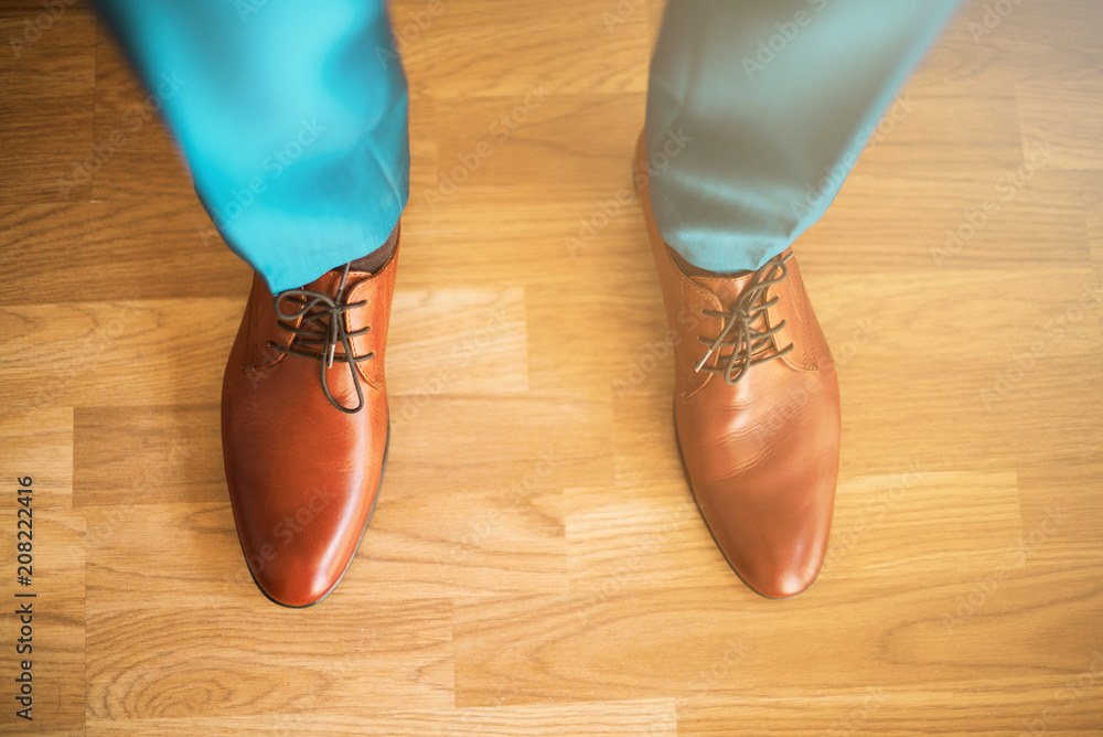 Man wearing shoes on wooden floor. Clothing concept, groom getting ready before ceremony. Body detail of businessman. Sunlight bokeh. Man wearing shoes on wooden floor. Clothing concept, groom getting ready before ceremony. Body detail of businessman. Sunlight bokeh.