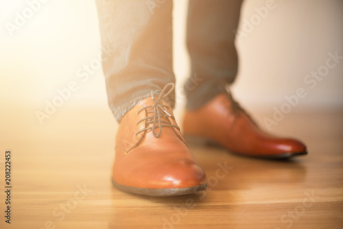 Man wearing shoes on wooden floor. Clothing concept, groom getting ready before ceremony. Body detail of businessman. Sunlight bokeh.