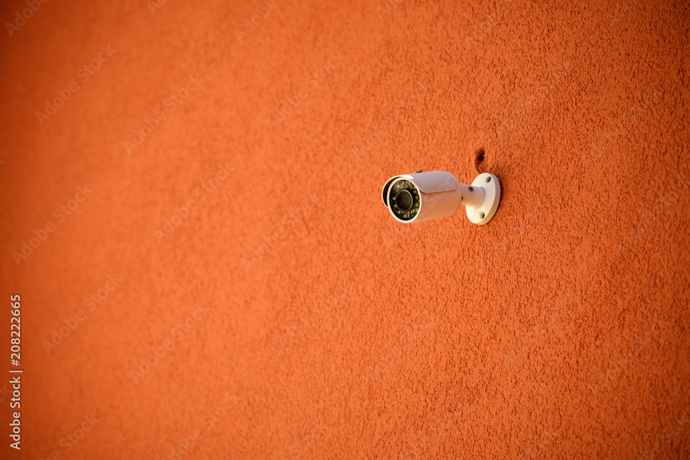close up view of security camera on orange colored building facade close up view of security camera on orange colored building facade