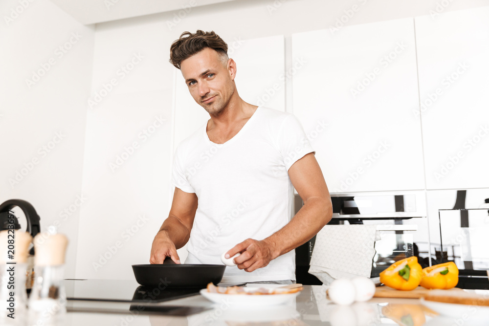 Smiling man cooking eggs for breakfast