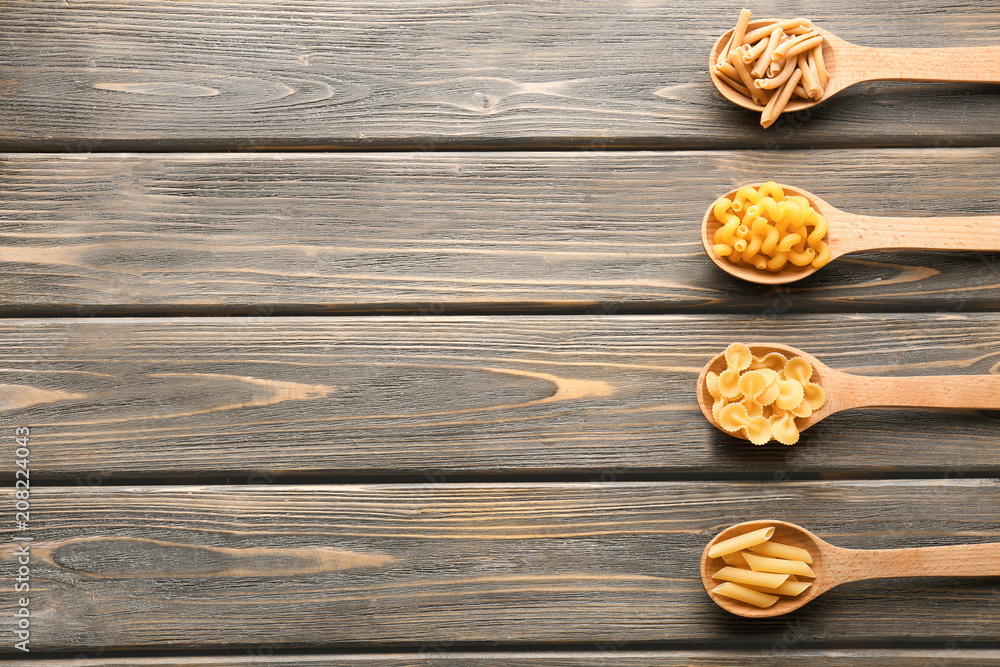 Naklejka premium Spoons with different uncooked pasta on wooden background