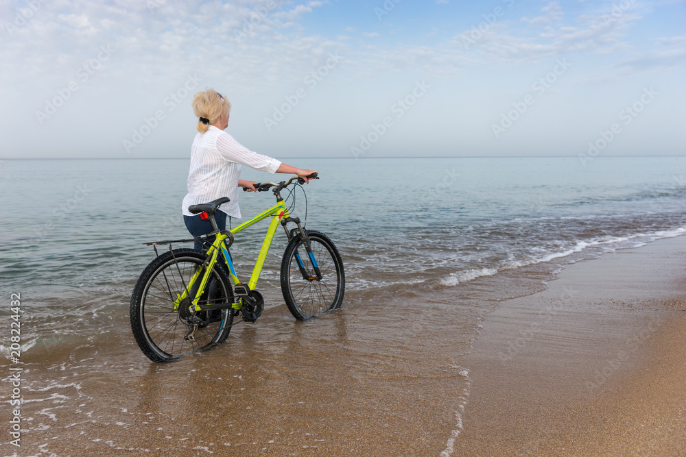 Fototapeta premium Woman walking in the sea wheeling a bicycle