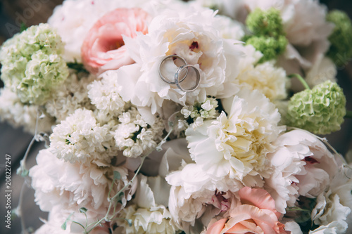 Close-up golden rings of newlyweds on flowers. A wedding bouquet of beautiful and fresh peonies lies on a wooden vintage table. The concept of wedding floristry and jewelry.