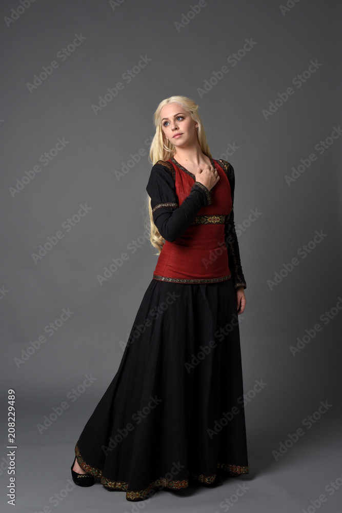 full length portrait of pretty blonde lady wearing a red and black fantasy medieval gown. standing pose on grey background. full length portrait of pretty blonde lady wearing a red and black fantasy medieval gown. standing pose on grey background.