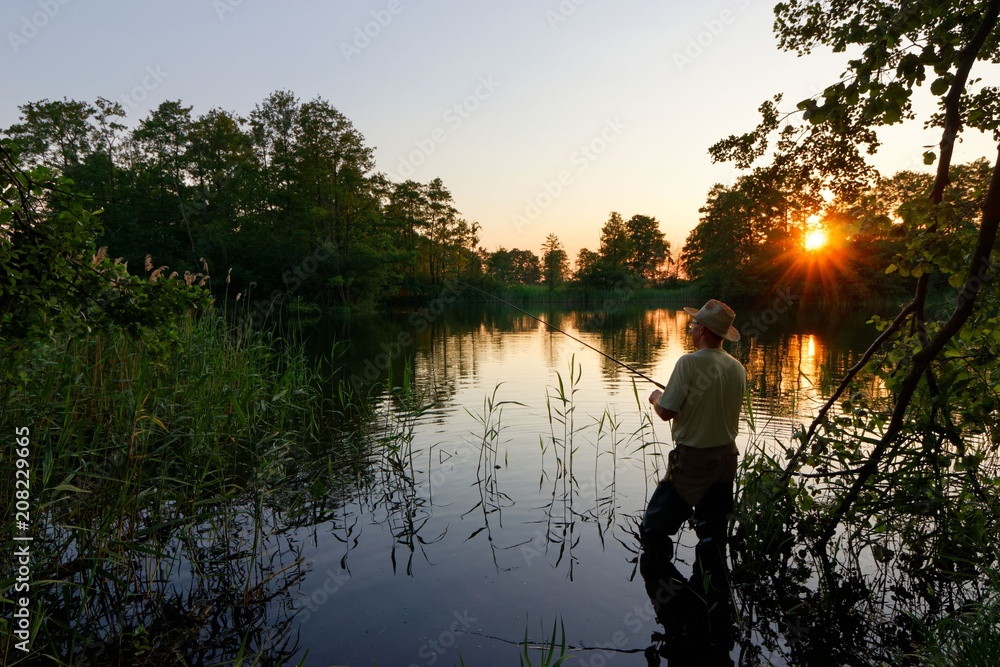 Fisherman standing in the lake and catching the fish during sunset