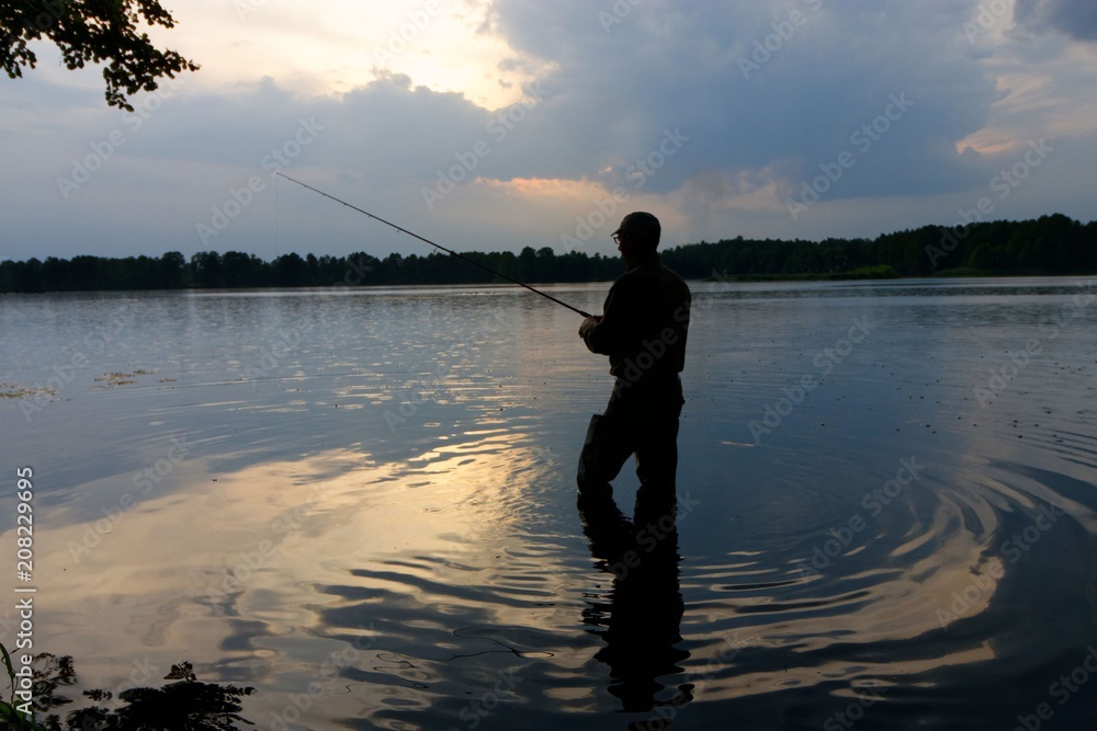 Fisherman standing in the lake and catching the fish during rain Fisherman standing in the lake and catching the fish during rain