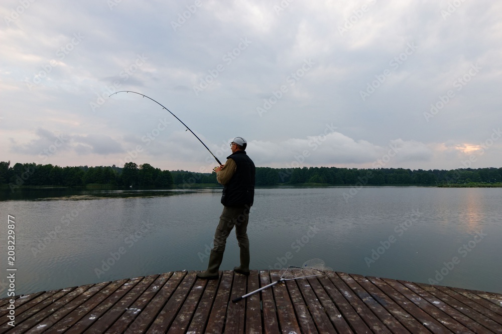 Fisherman catching the fish from wooden pier during cloudy day Fisherman catching the fish from wooden pier during cloudy day