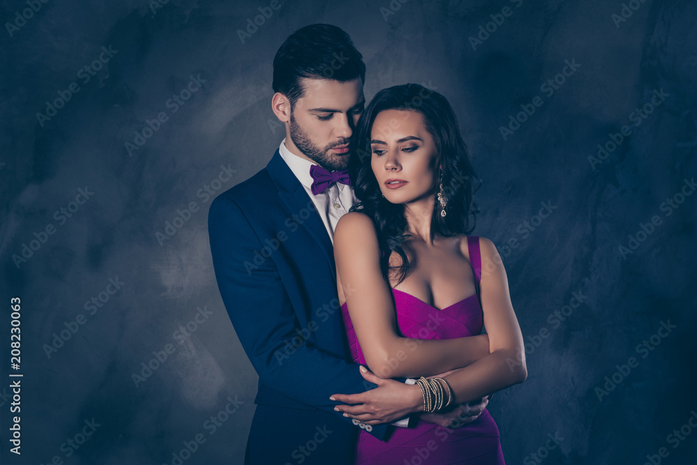 Portrait of pretty charming mrs in purple dress with jewelry half face mr in tuxedo bowtie holding hand in pocket of pants embracing his lover lovely attractive couple isolated on grey background - obrazy, fototapety, plakaty 