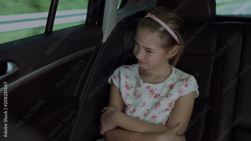 Portrait of cheerful lovely girl with folded hands looking through car window while sitting in the back seat of the car during travel. Positive cute child enjoying road trip while riding in the car. Portrait of cheerful lovely girl with folded hands looking through car window while sitting in the back seat of the car during travel. Positive cute child enjoying road trip while riding in the car.