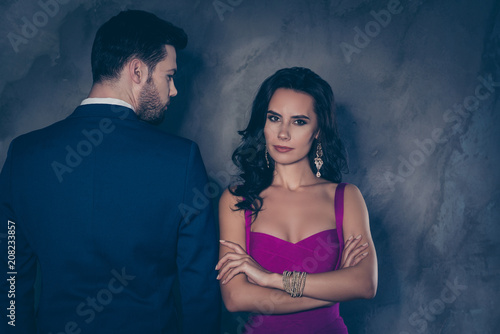 Portrait of pretty charming mrs in purple dress with jewelry half face mr in tuxedo bowtie holding hand in pocket of pants embracing his lover lovely attractive couple isolated on grey background © deagreez