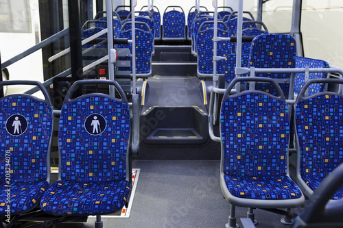 Bus inside, city transportation interior with blue seats in row, retirement places, open doors, handles for standing passengers 