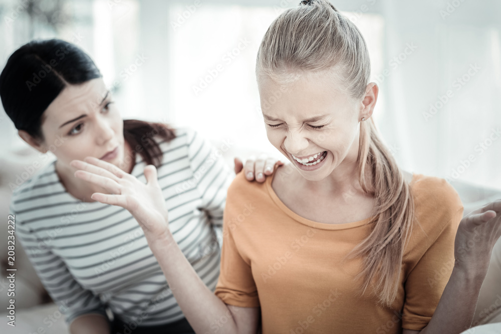 Free your emotions. Attractive teen girl screaming while professional female psychologist gazing at her and posing on blurred background Free your emotions. Attractive teen girl screaming while professional female psychologist gazing at her and posing on blurred background