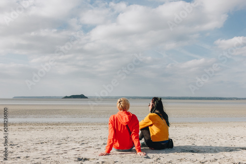 back view of girls sitting on sandy beach, Saint michaels mount, Normandy, France