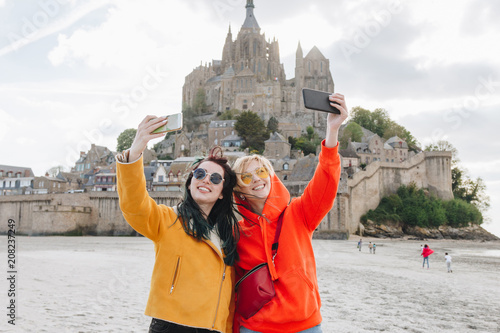 smiling tourists taking selfie on smartphone near Saint michaels mount, Normandy, France