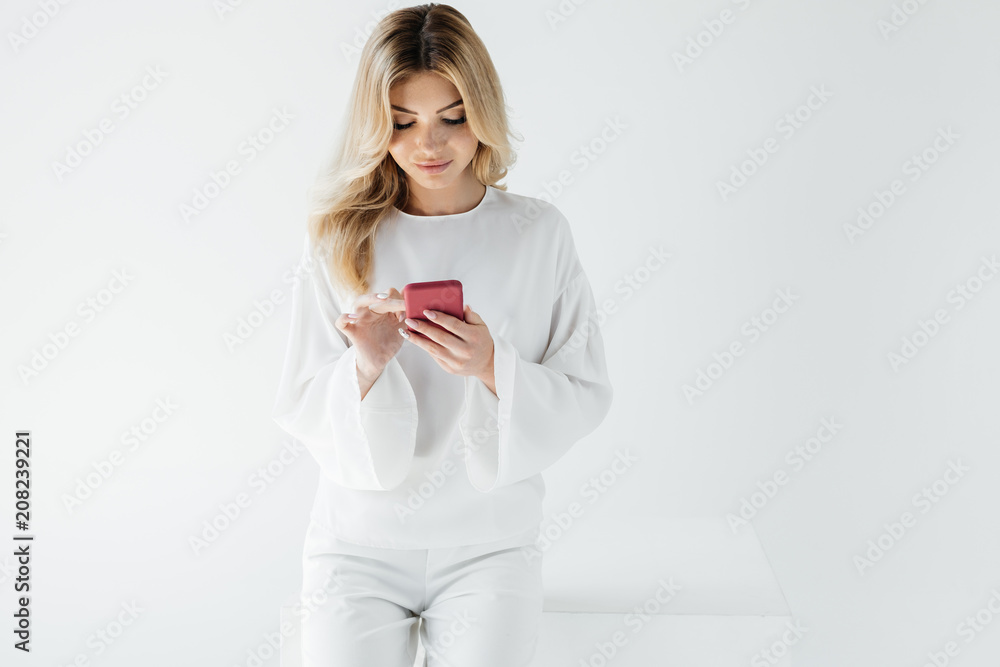portrait of blond woman in white clothing using smartphone isolated on grey portrait of blond woman in white clothing using smartphone isolated on grey