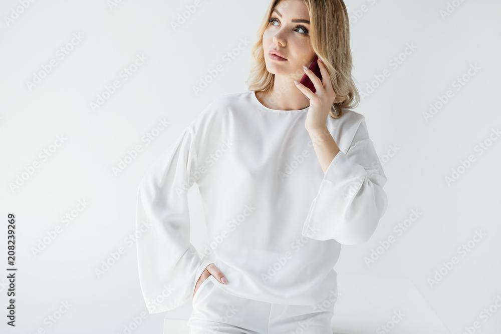 portrait of blond woman in white clothing talking on smartphone isolated on grey portrait of blond woman in white clothing talking on smartphone isolated on grey
