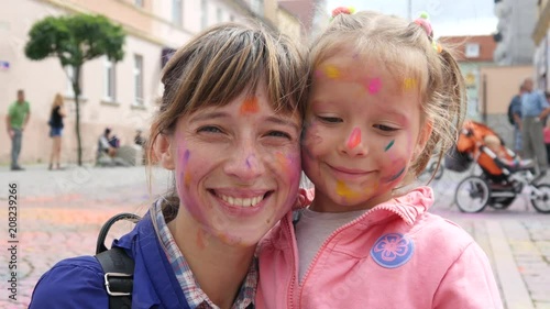 Mother and child daughter happy smile with face paint body art after sprinkle colored powder festival photo