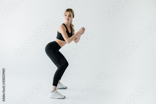 Side view of young athletic sportswoman squating isolated on grey
