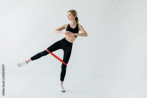 young athletic woman exercising with rubber tape isolated on grey