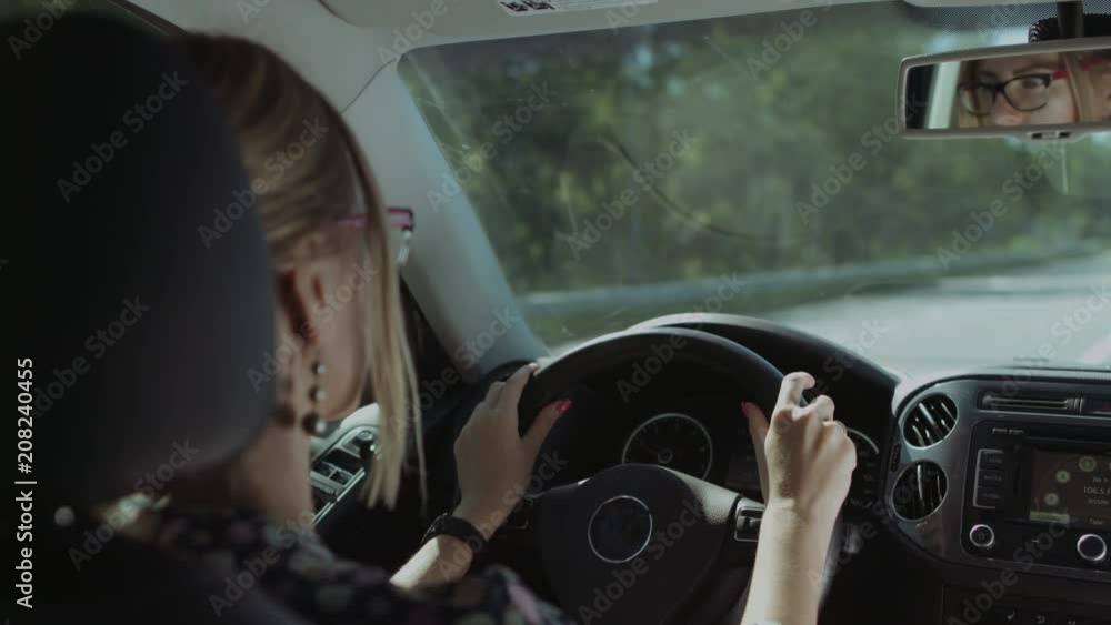 Gorgeous long blonde hair female driver is reflected in car rear view mirror while driving on highway. Beautiful woman driving car on freeway during summer vacation road trip. Gorgeous long blonde hair female driver is reflected in car rear view mirror while driving on highway. Beautiful woman driving car on freeway during summer vacation road trip.
