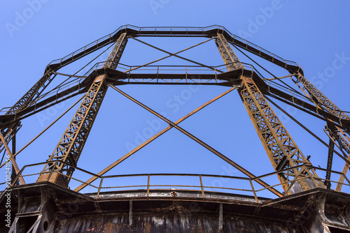 Photos Detail of olf vintage historic rusty steel gas holder with blue sky in the backg