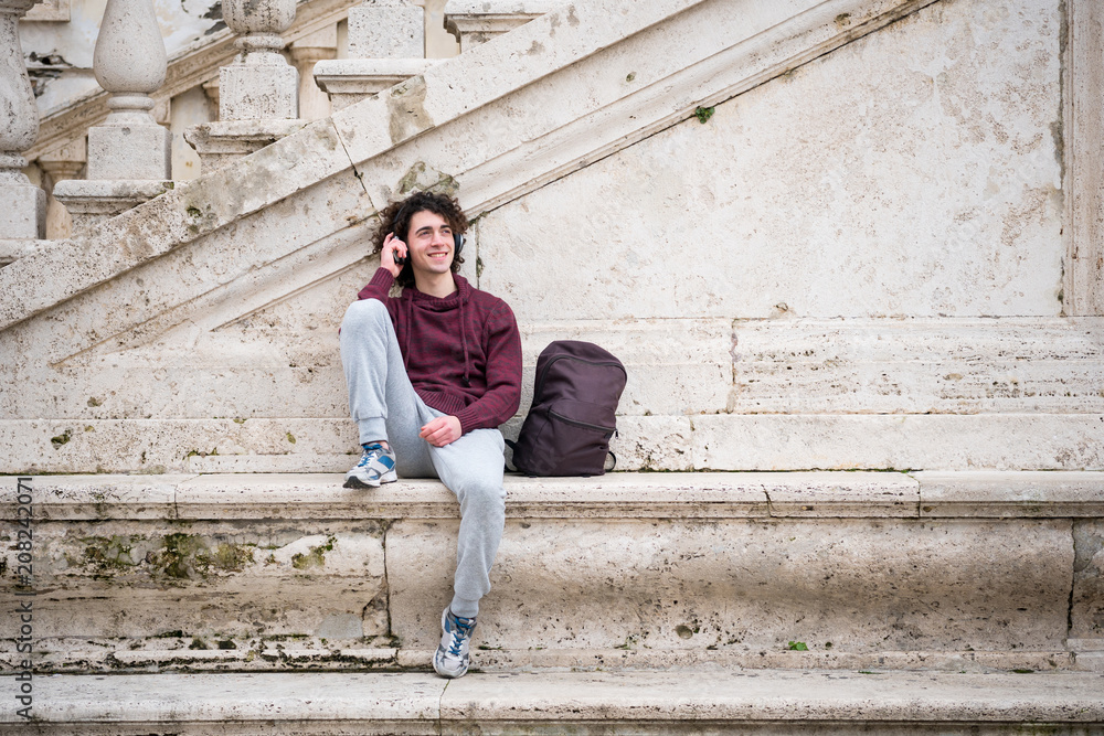 Handsome young man listening to music with headphones on his head. Young man relaxing in front of stone wall